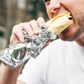 cropped view of man eating doner kebab in aluminium foil